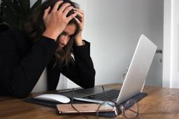 Image of a woman at a laptop with her head in her hands